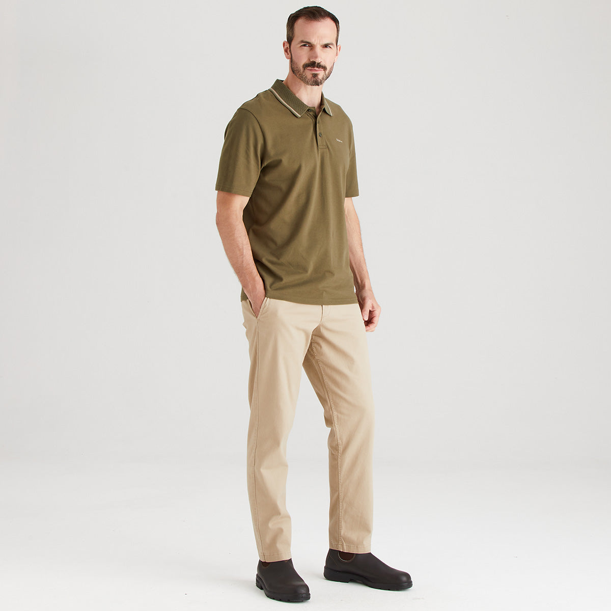 Man wearing a green polo shirt and beige pants on a white background