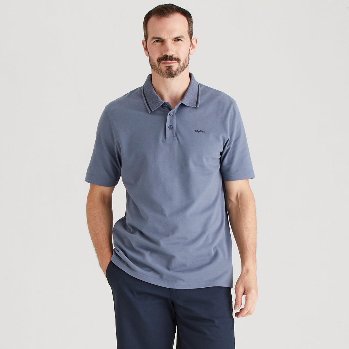 Man wearing a blue polo shirt with a brand logo on a light gray background