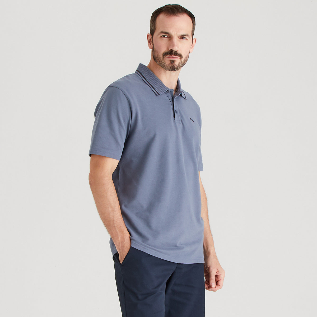 Man wearing a light blue polo shirt and dark pants on a gray background