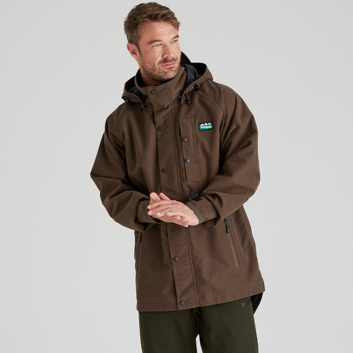 Man wearing a brown waterproof jacket with a visible Ridgeline Clothing brand logo on a grey background