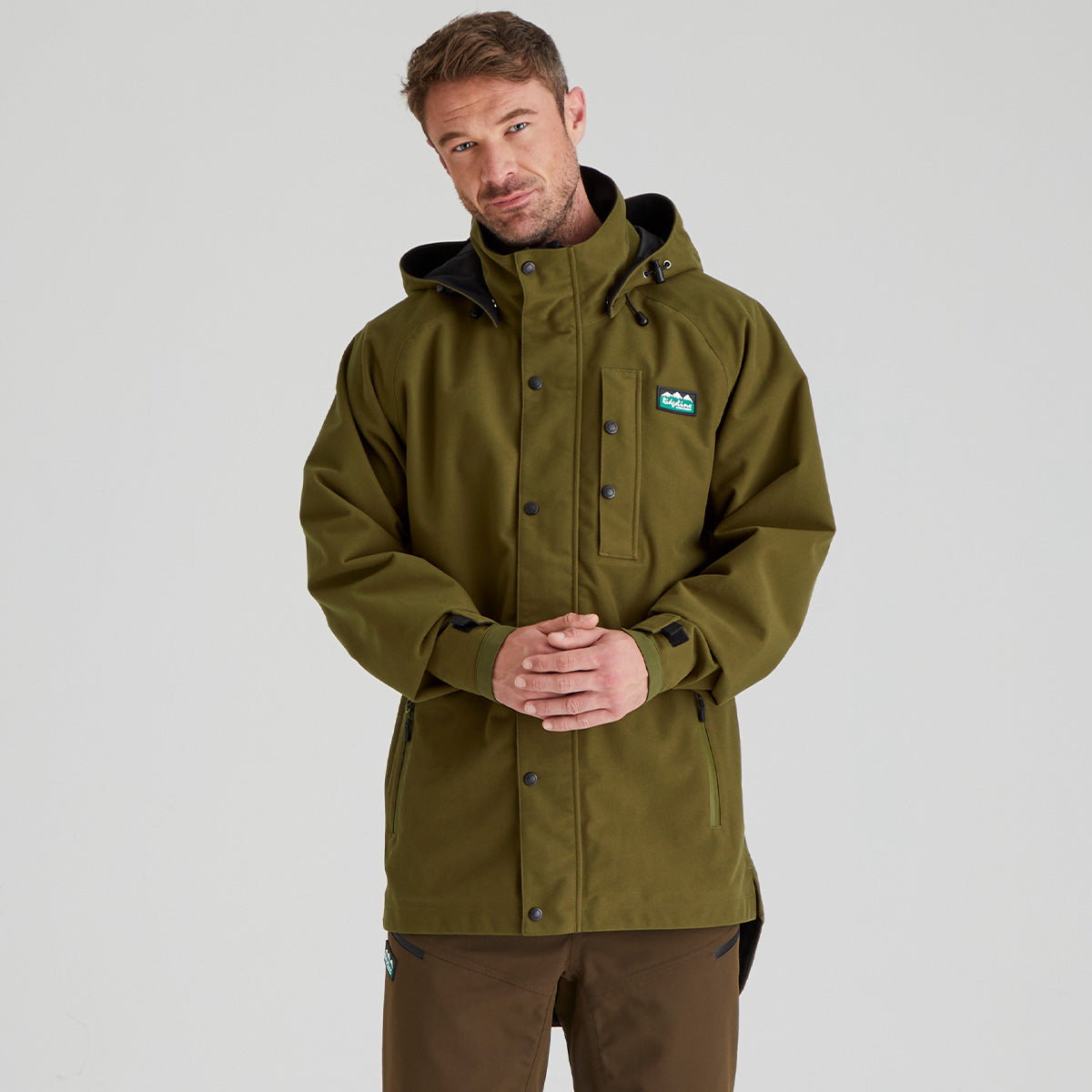 Man wearing a Brown waterproof jacket with a brand logo on a grey background