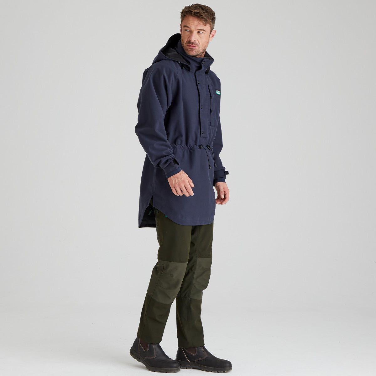 Man wearing a navy raincoat and green pants on a light gray background