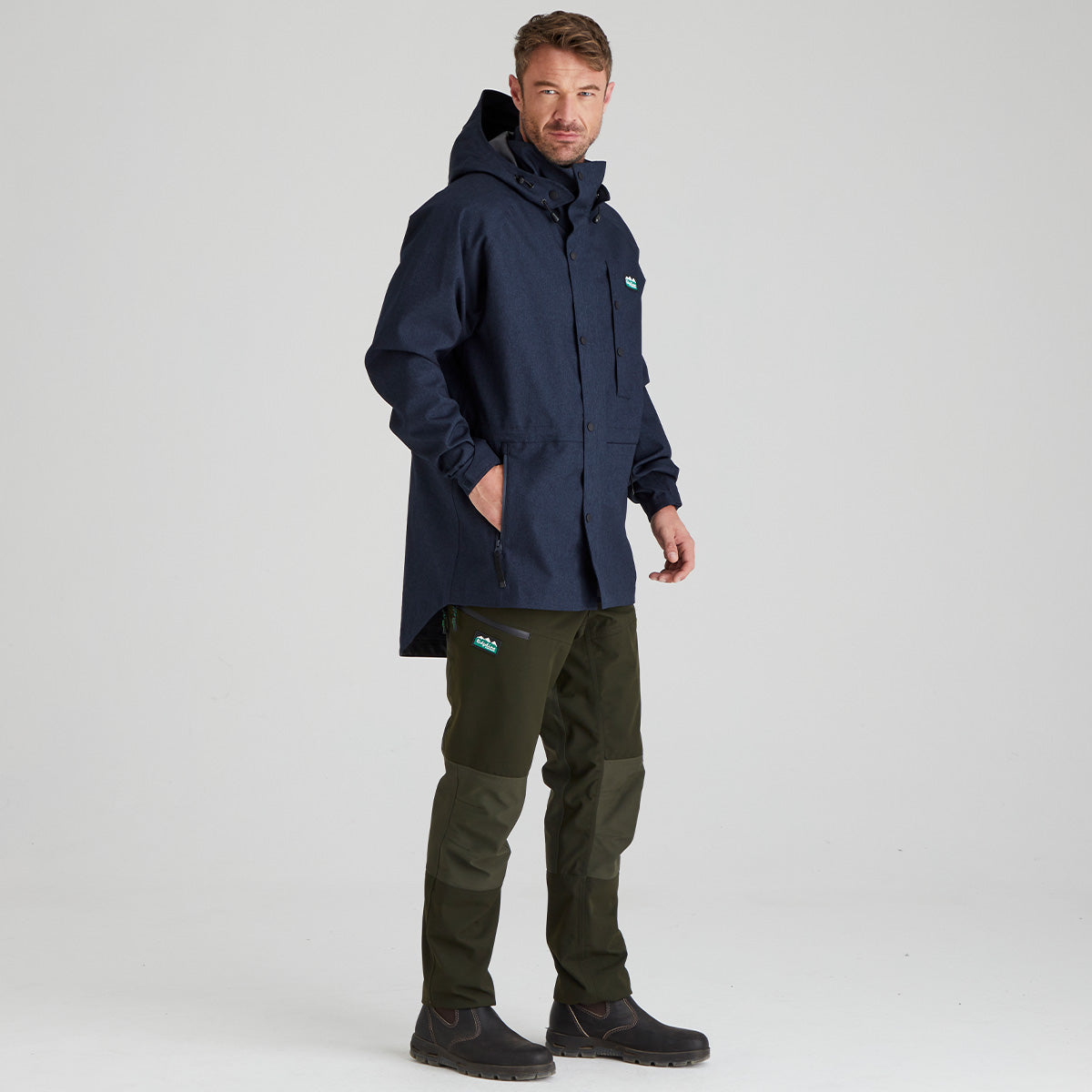 Man wearing a navy raincoat and green pants on a light gray background