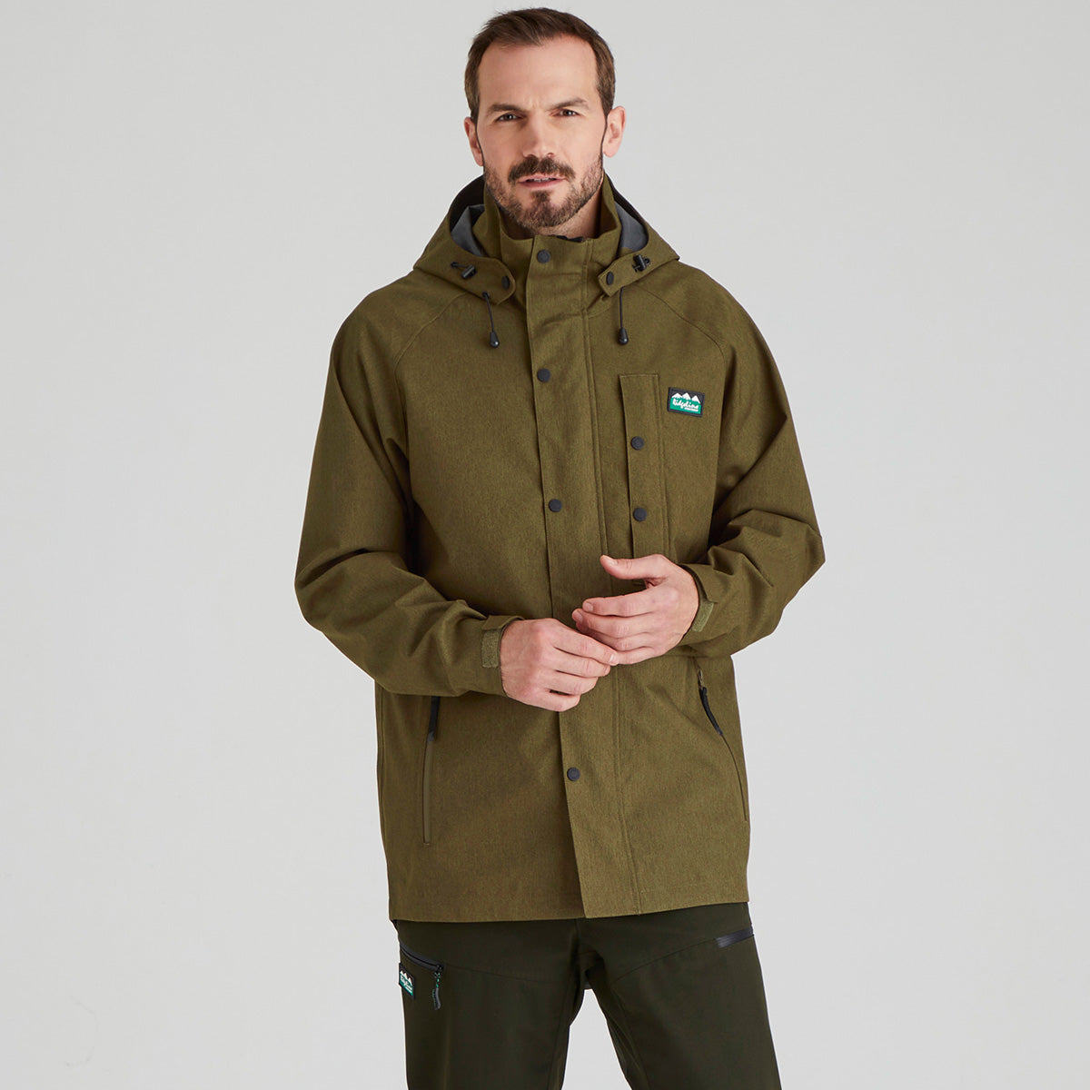 Man wearing a green jacket with a brand logo on a light grey background