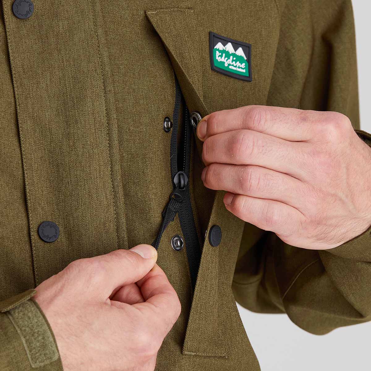 Close-up of a person opening a zipped pocket of a green jacket with a visible brand logo.