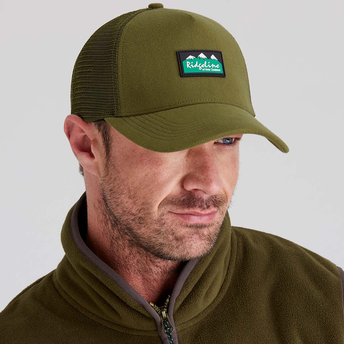 Man wearing a green cap with a logo on a gray background