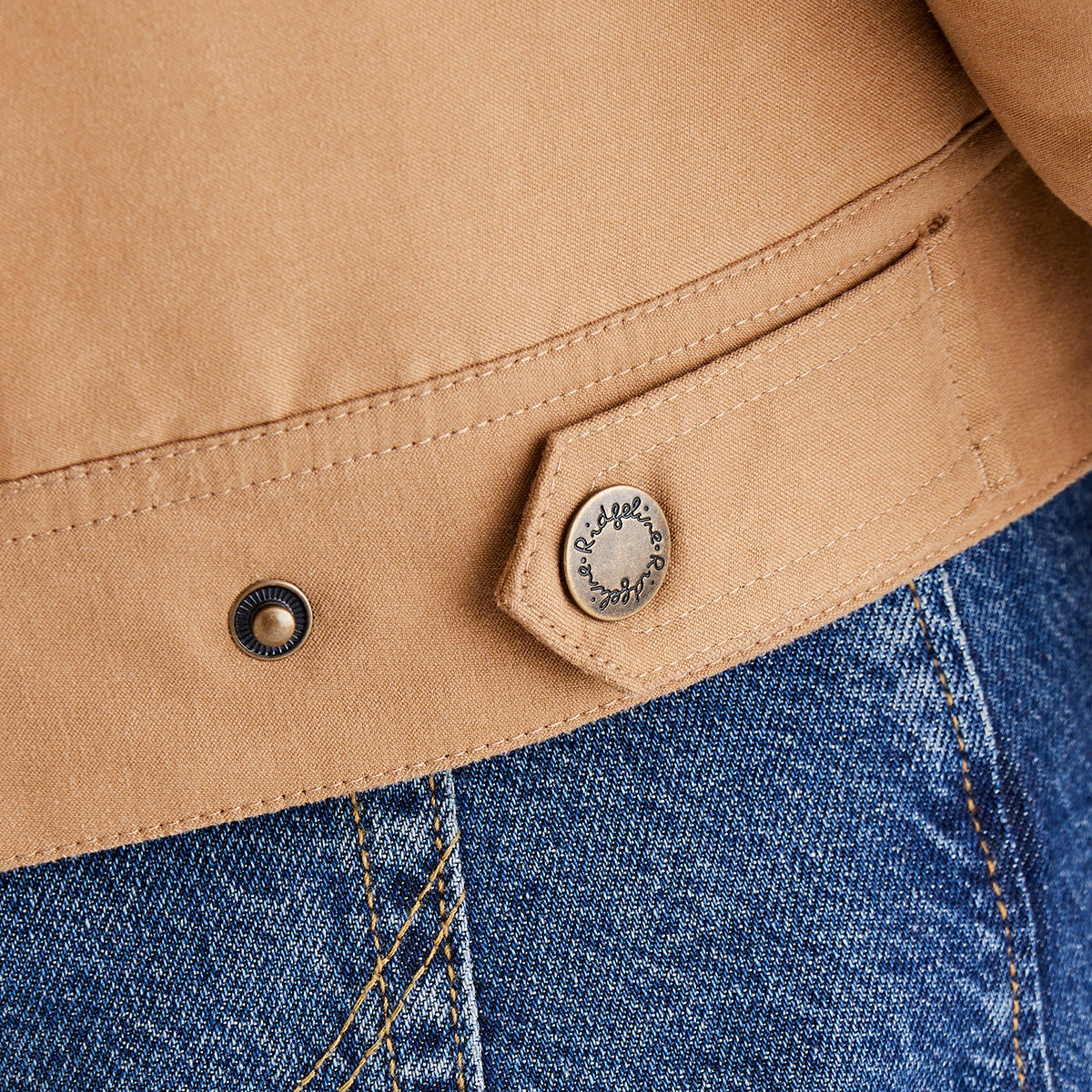 Close-up of a beige jacket button and blue jeans fabric