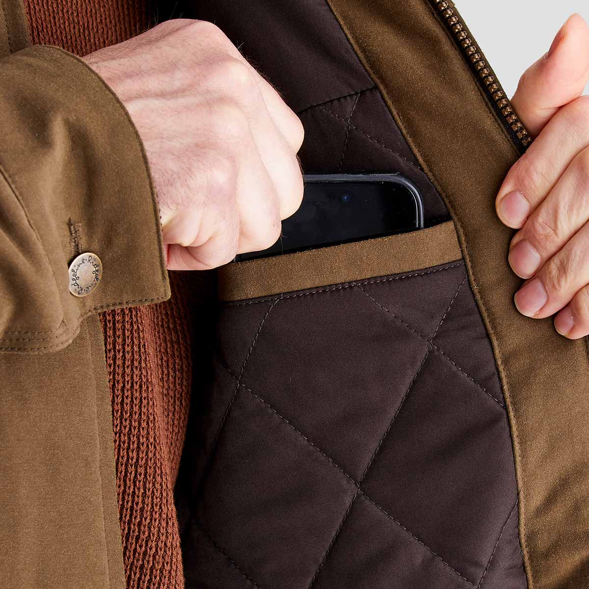 Person wearing a brown quilted jacket with a phone in the pocket.