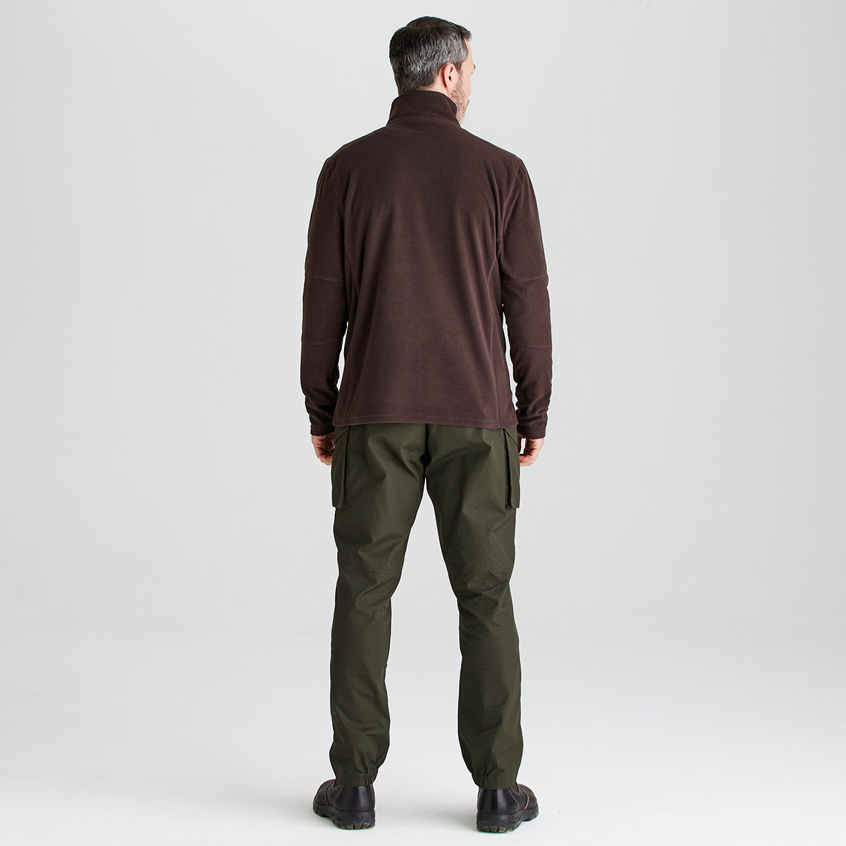 Man wearing a brown long-sleeve shirt and green pants on a light gray background