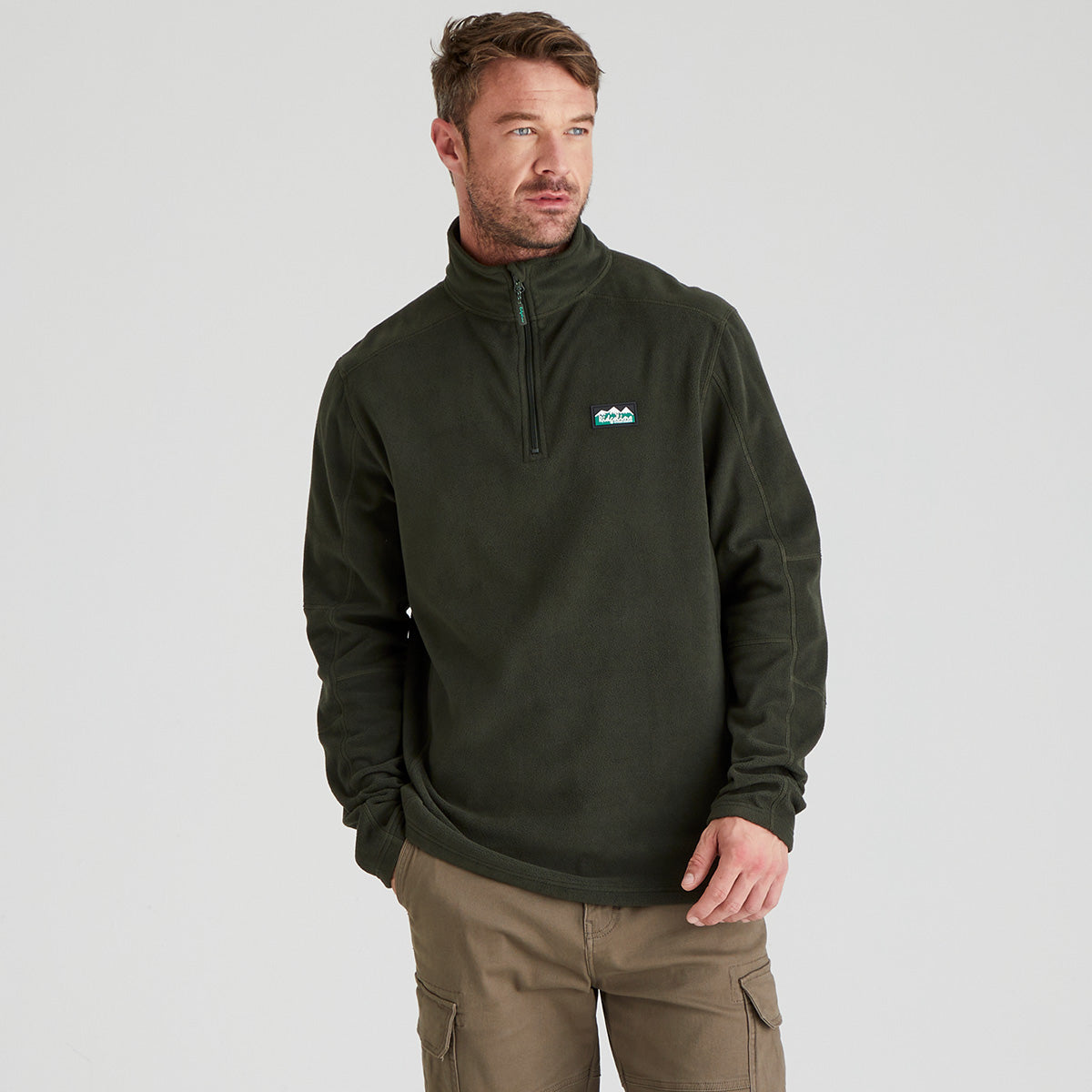 Man wearing a dark green fleece pullover with a ridgeline clothing logo on a light grey background