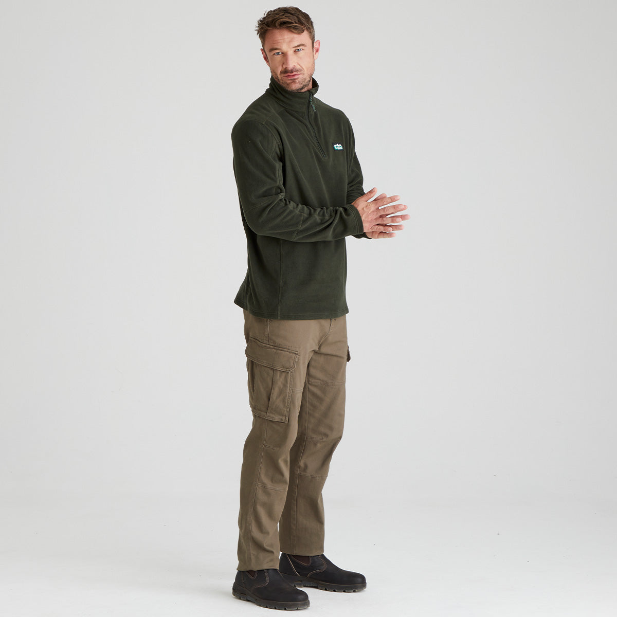 Man wearing a green fleece pullover  and cargo pants on a grey background