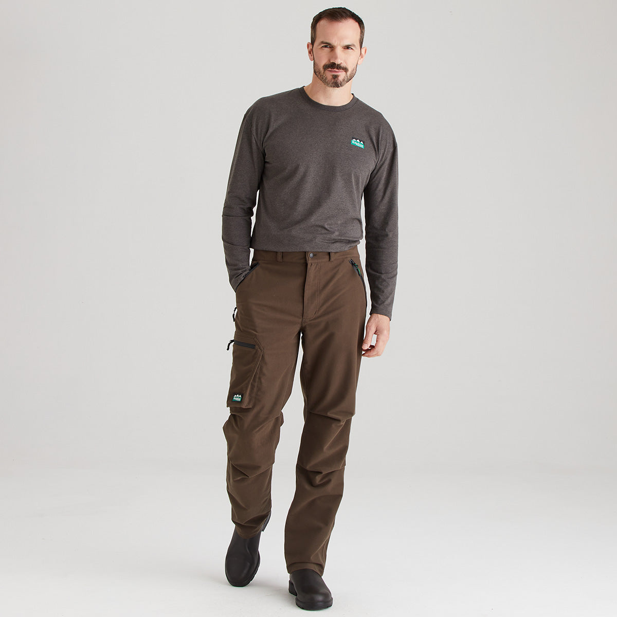 Man wearing a gray long-sleeve shirt and brown pants on a white background