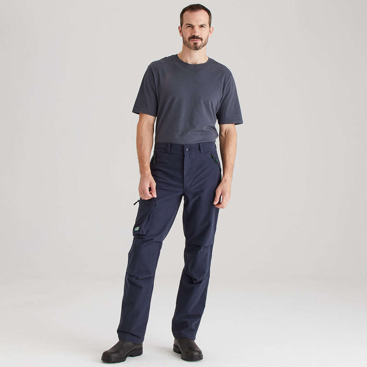 Man wearing a dark gray t-shirt and navy pants on a light gray background