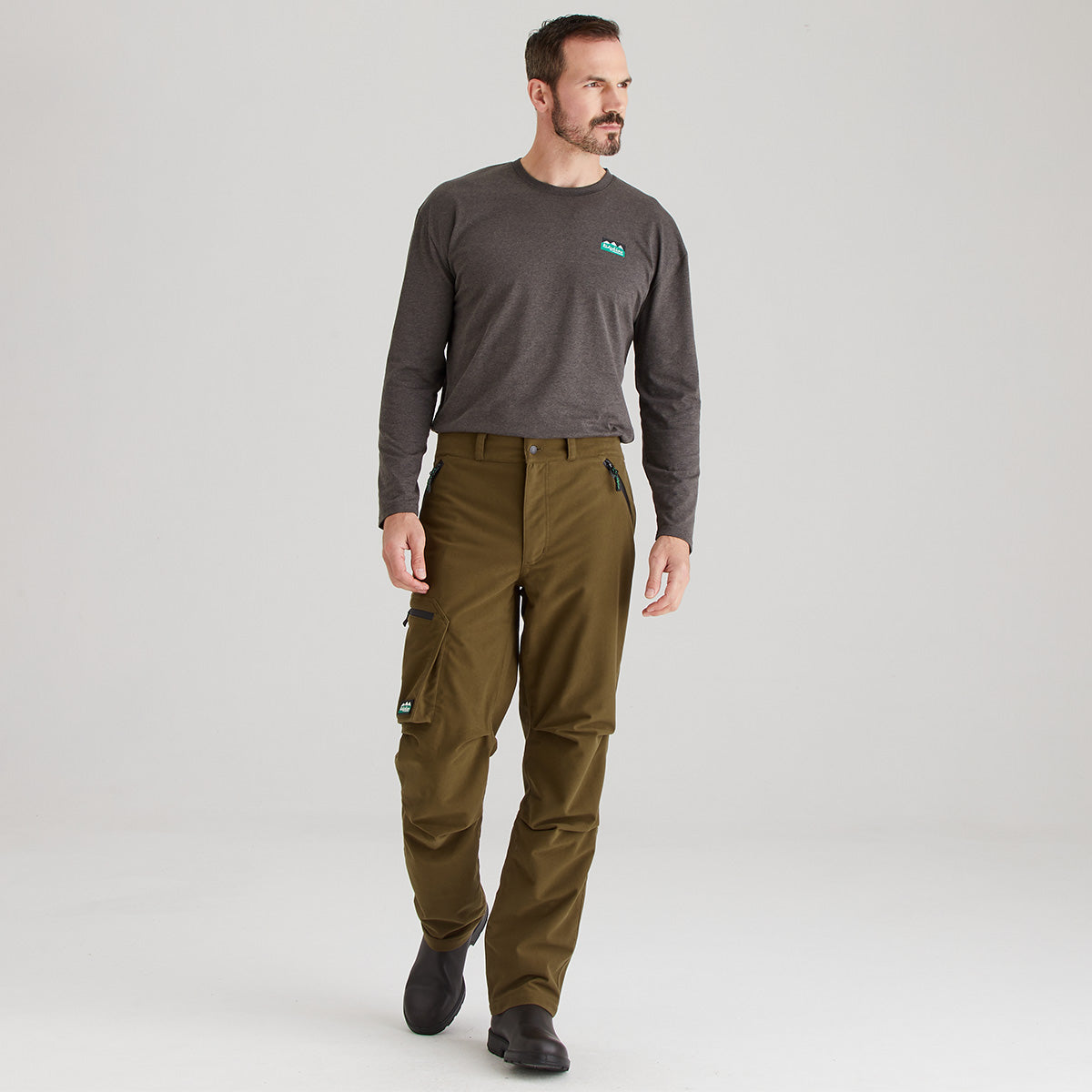 Man wearing a dark gray long-sleeve shirt and green pants on a light gray background