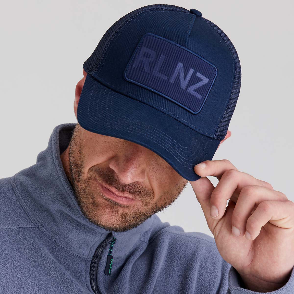 Man wearing a navy blue cap with 'RLNZ' logo on a light grey background