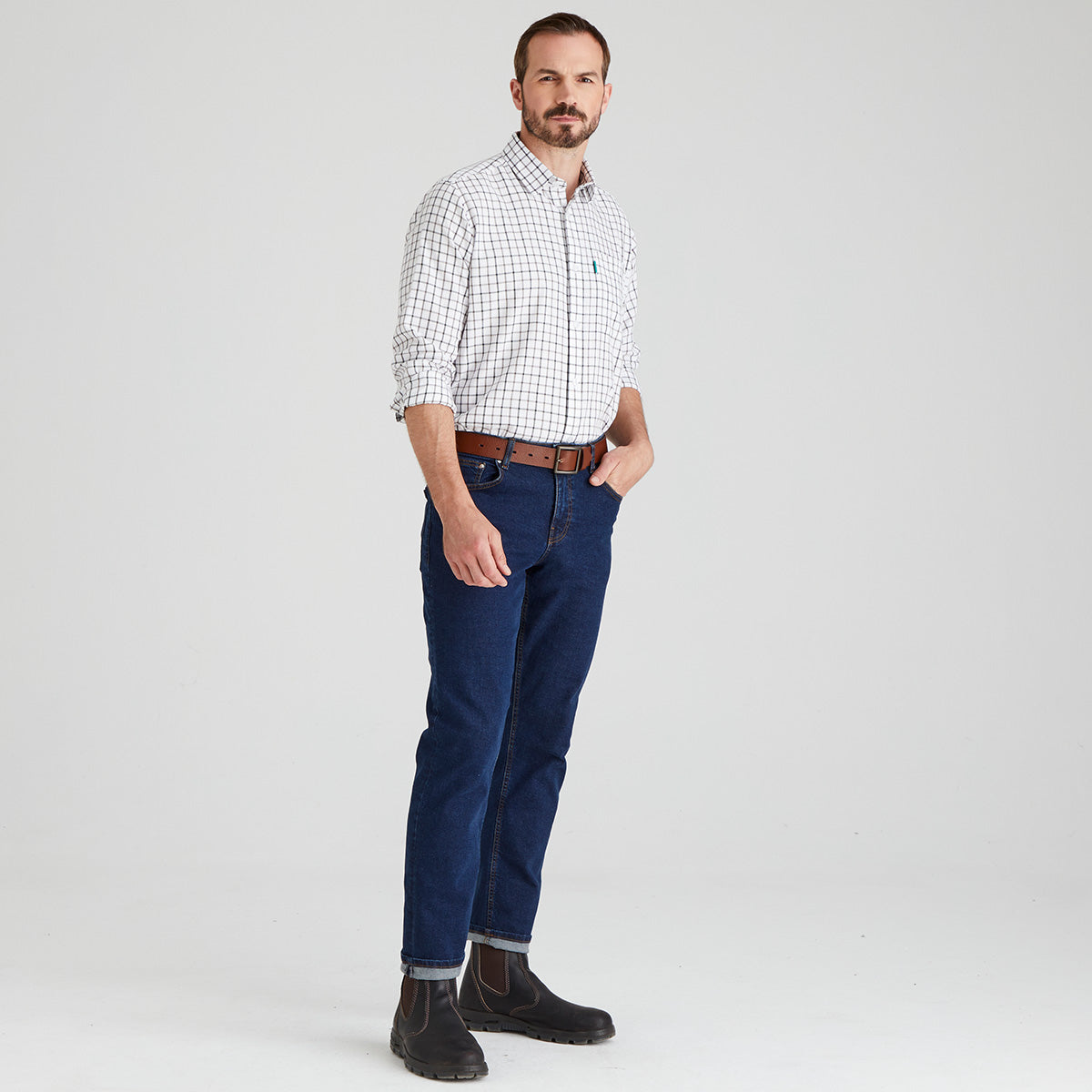 Man wearing a checkered shirt, blue jeans, and black shoes on a light grey background