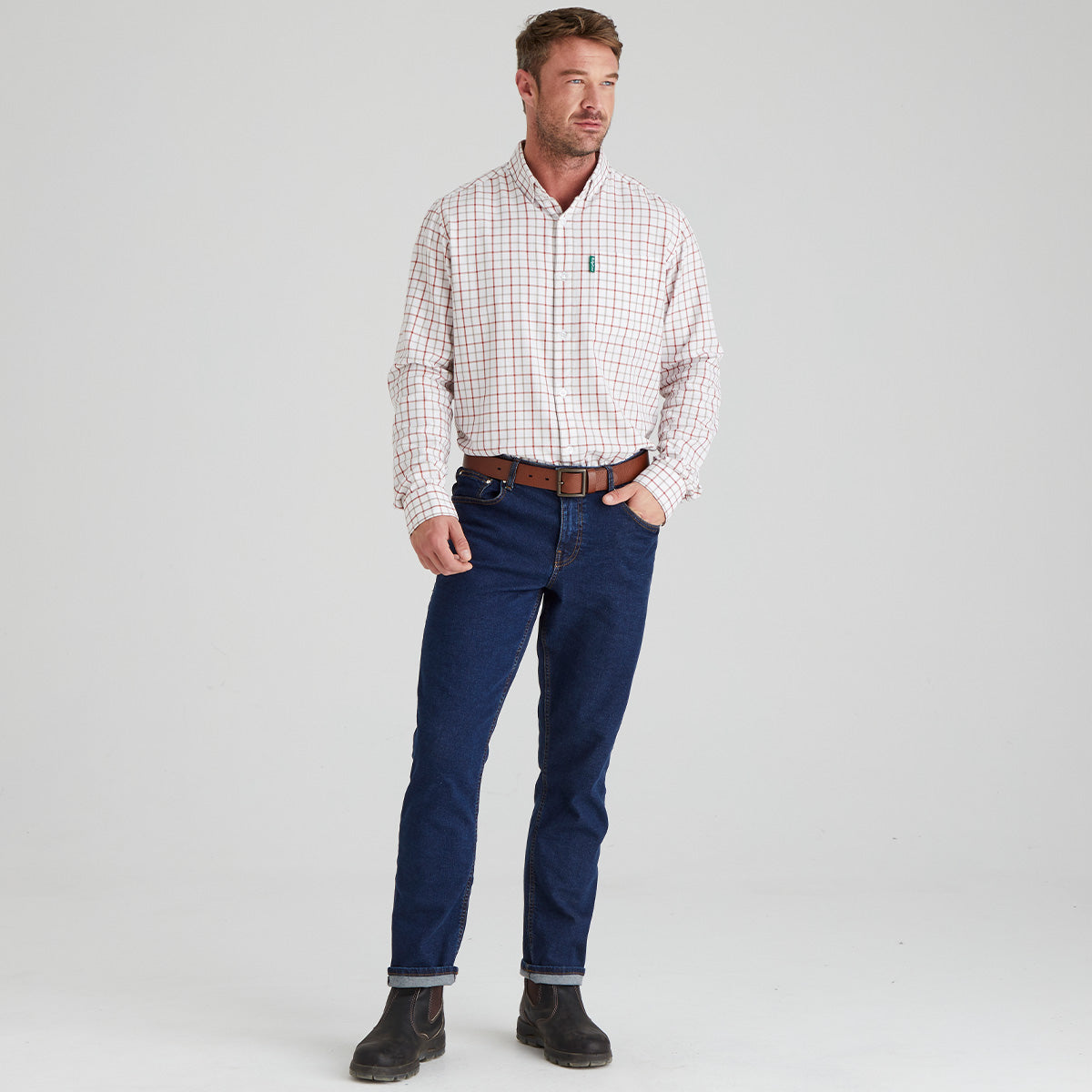 Man wearing a checkered shirt, blue jeans, and black boots on a light grey background