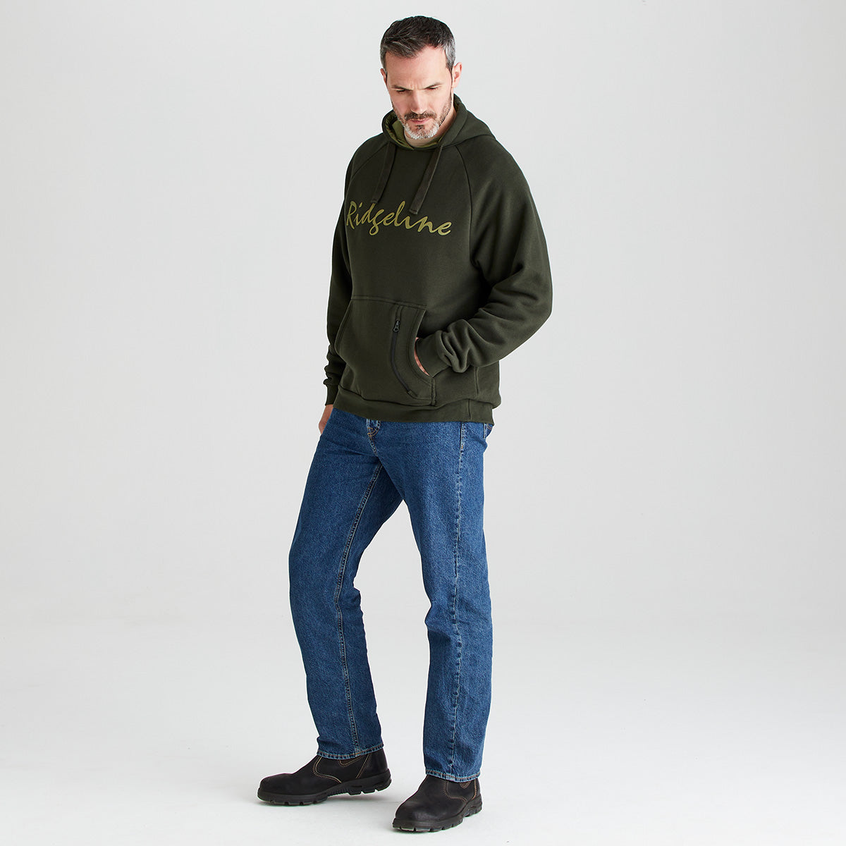 Man wearing a green hoodie with text and blue jeans on a white background