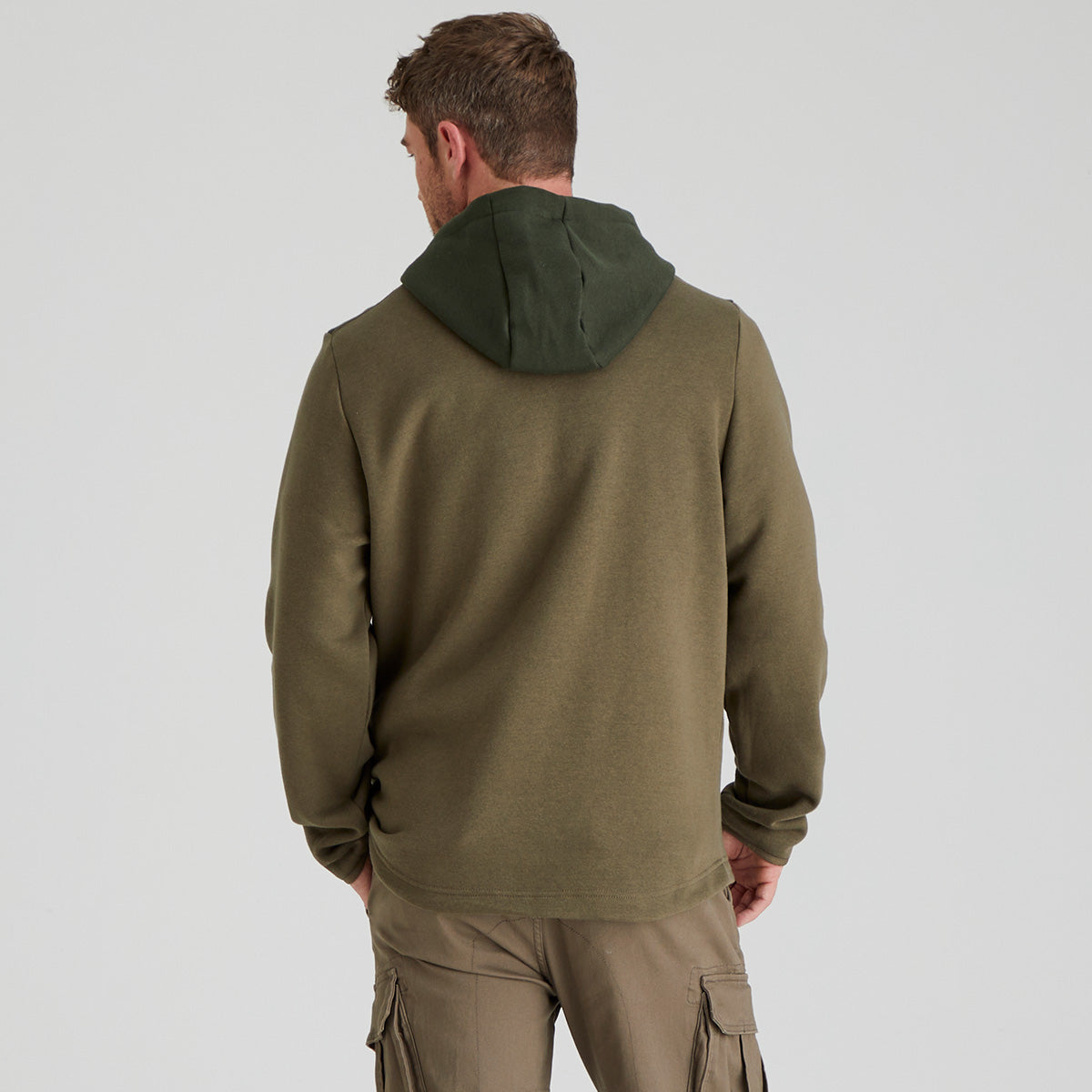 back view of man wearing a green hoodie and cargo pants on a light grey background