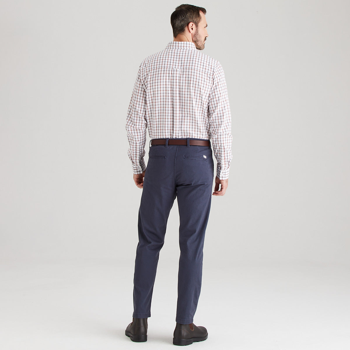 Man wearing a checkered shirt and navy pants on a light gray background
