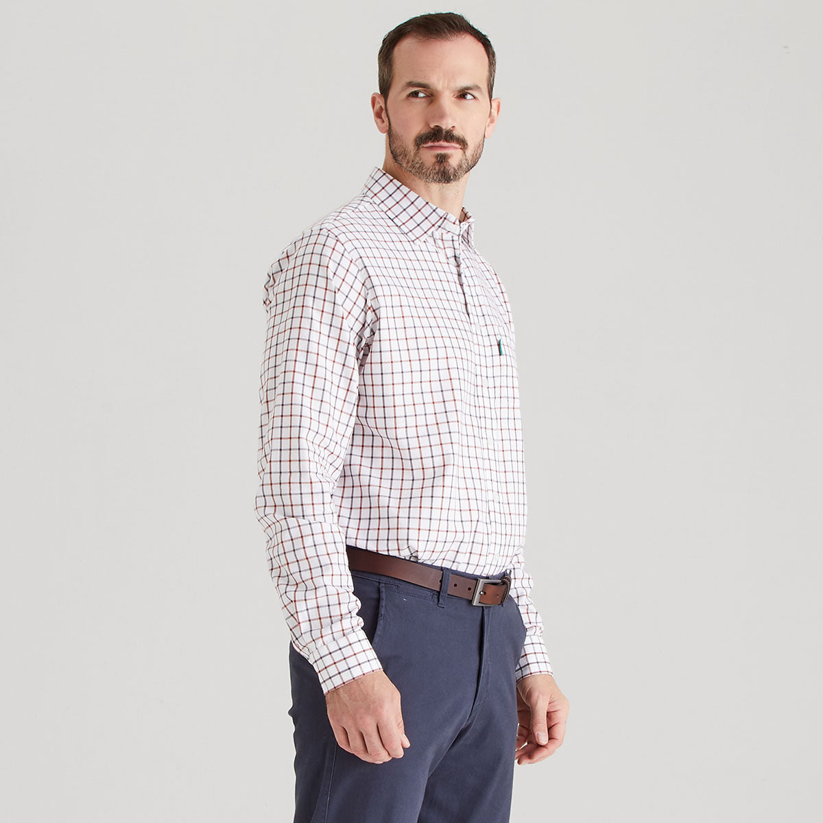 Man wearing a checkered shirt and dark pants on a light gray background