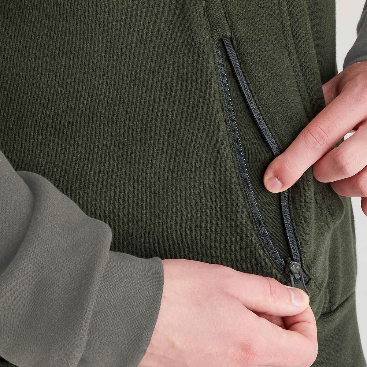 Olive green hoodie zip pocket detail with contrast grey sleeve and concealed zip fastening, close-up view.