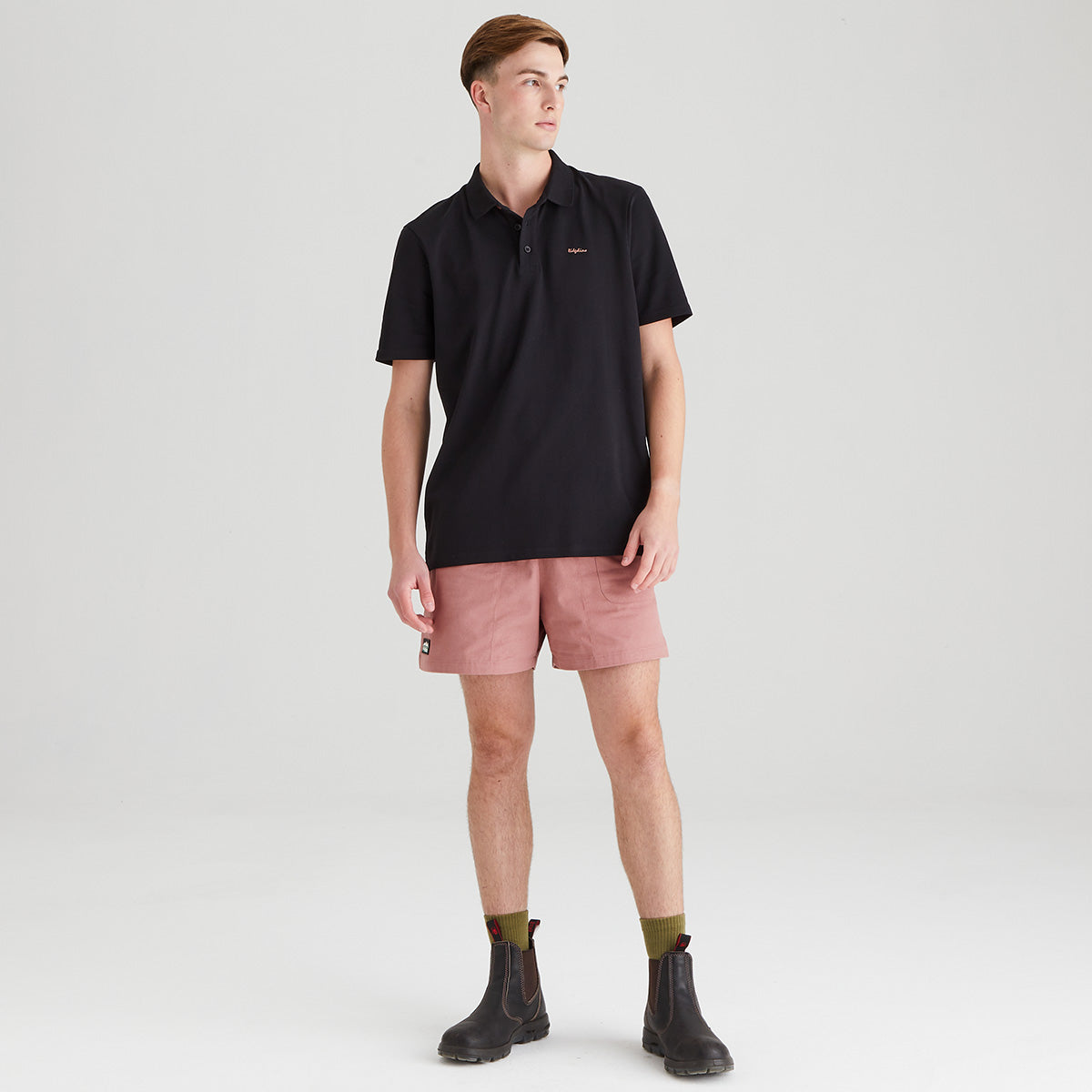 Person wearing a black polo shirt and pink shorts on a light gray background