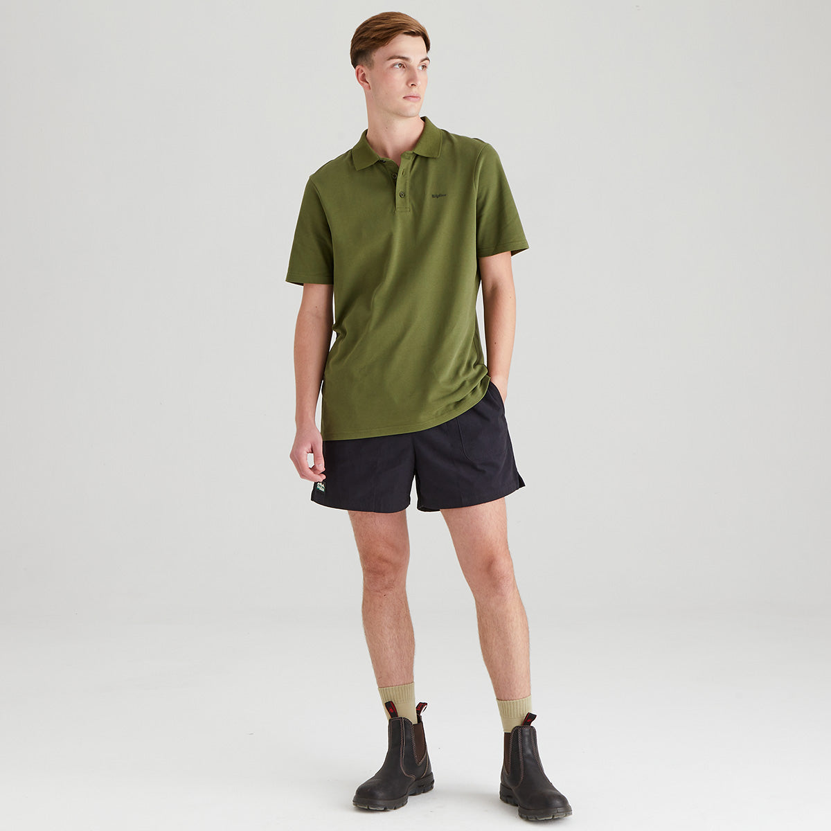 Man wearing a green polo shirt and black shorts on a white background