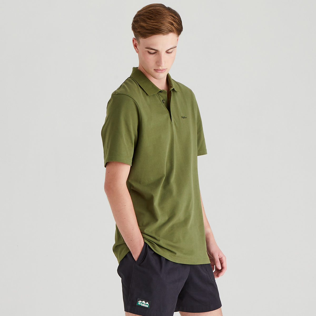 Person wearing a green polo shirt and black shorts on a light gray background