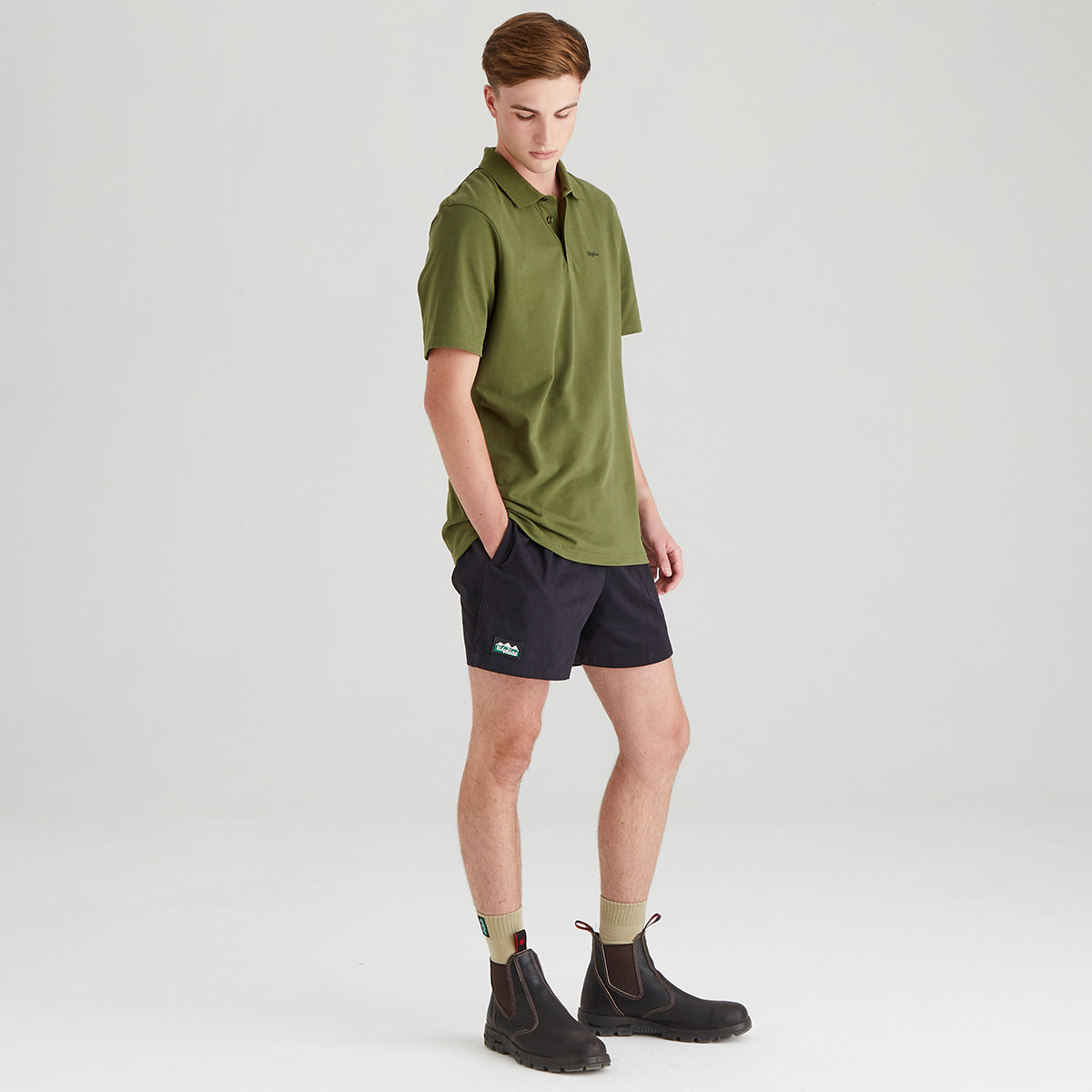 Man wearing a green polo shirt and black shorts on a light gray background