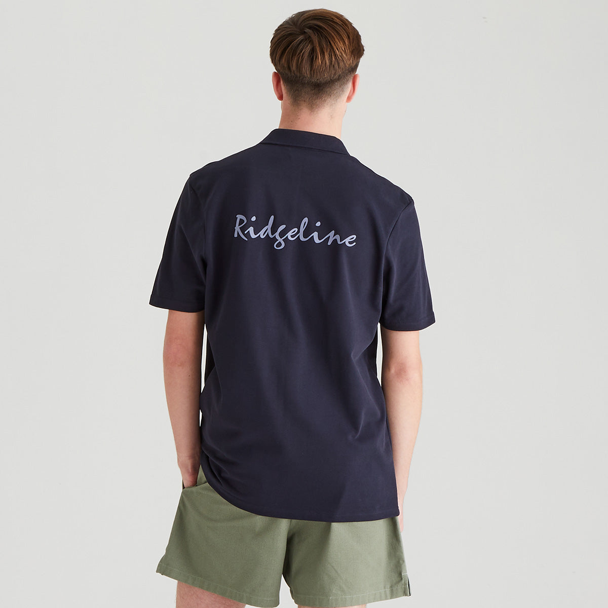 Person wearing a navy blue polo shirt with 'Ridgeline' branding on the back, standing against a light gray background.