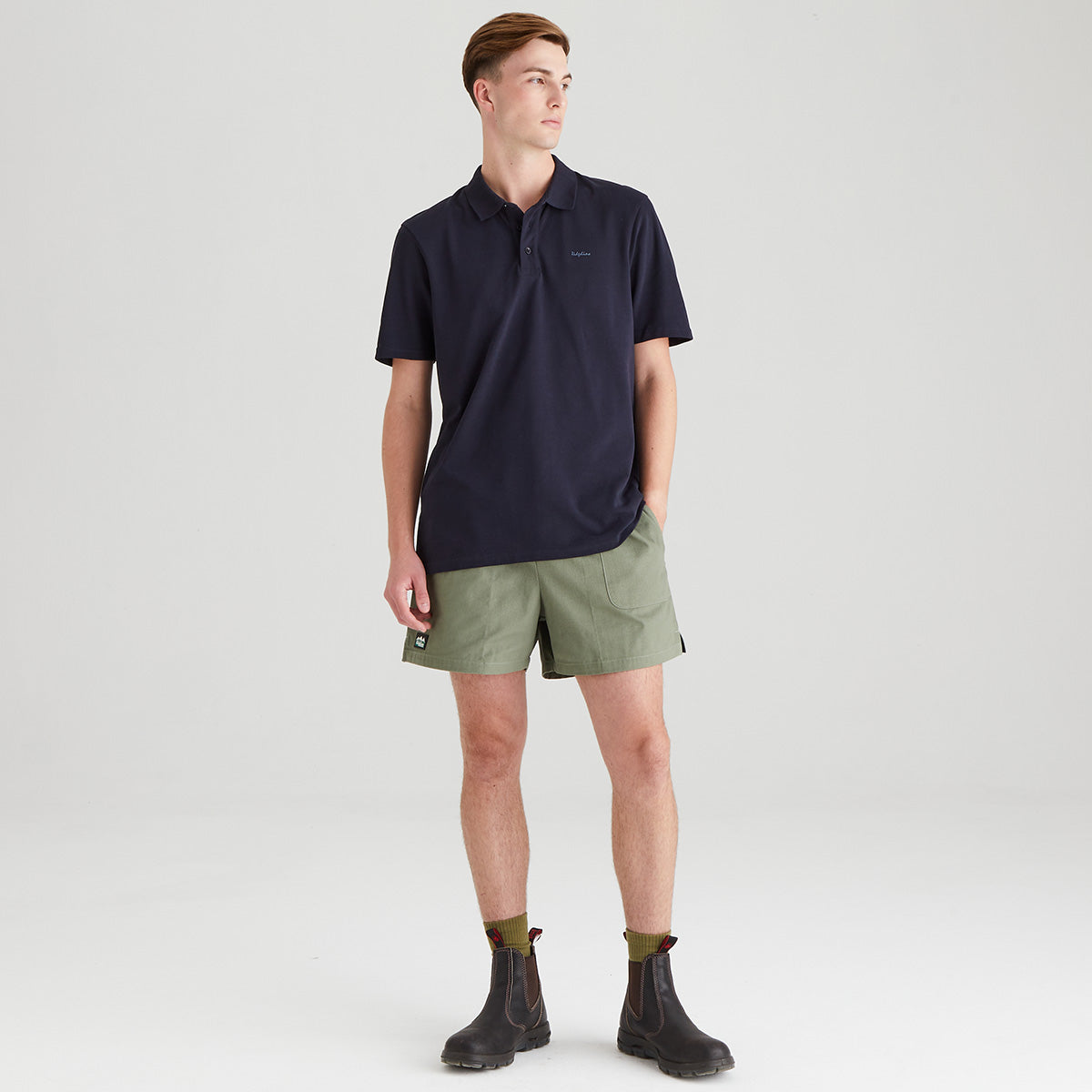 Man wearing a navy polo shirt and green shorts on a light gray background