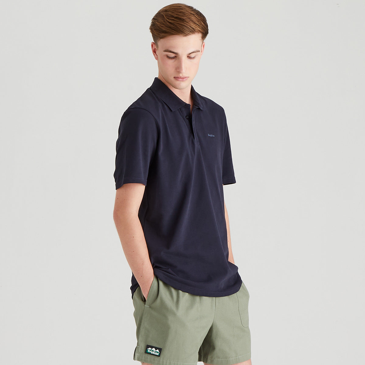 Man wearing a navy polo shirt and green shorts on a light gray background