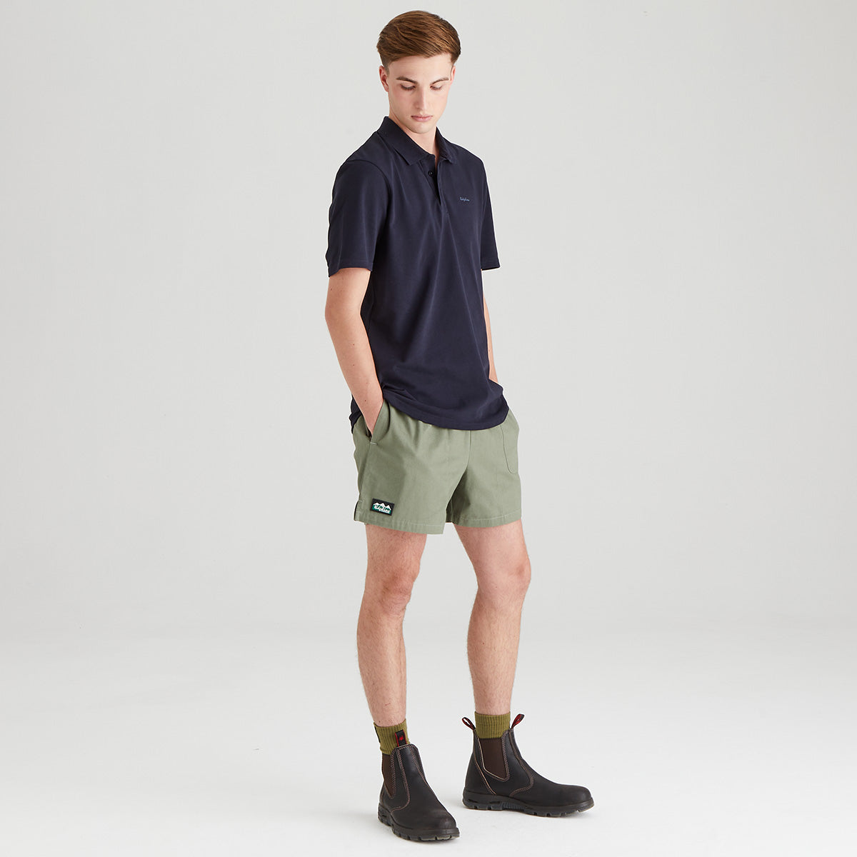 Man wearing a navy polo shirt and green shorts on a light gray background