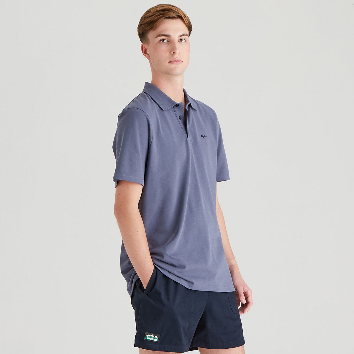 Person wearing a blue polo shirt and navy shorts on a light gray background