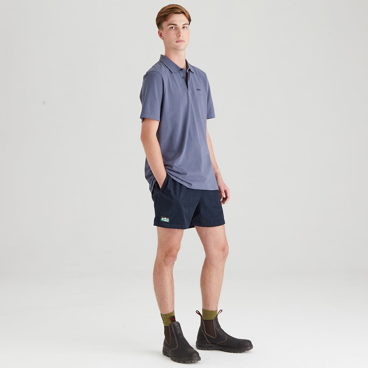 Man wearing a blue polo shirt and navy shorts on a white background