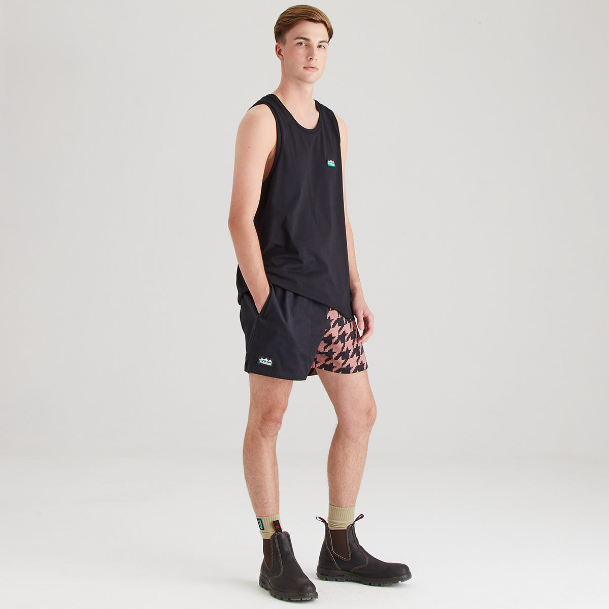 Person wearing a black sleeveless shirt and patterned shorts on a light gray background