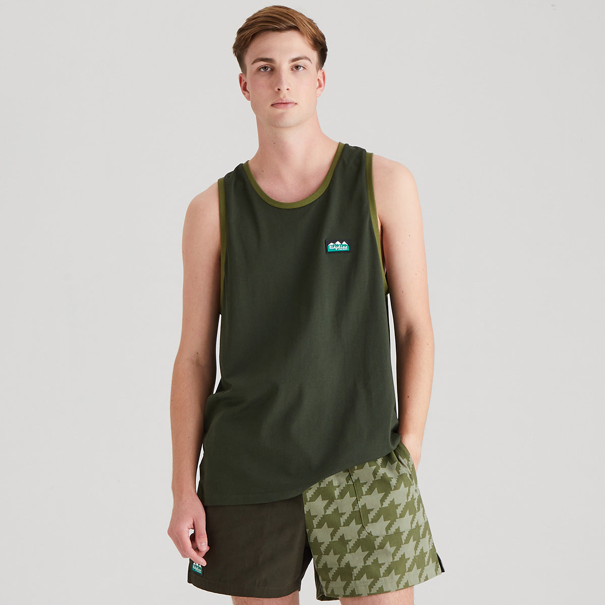 Person wearing a green tank top and patterned shorts on a gray background