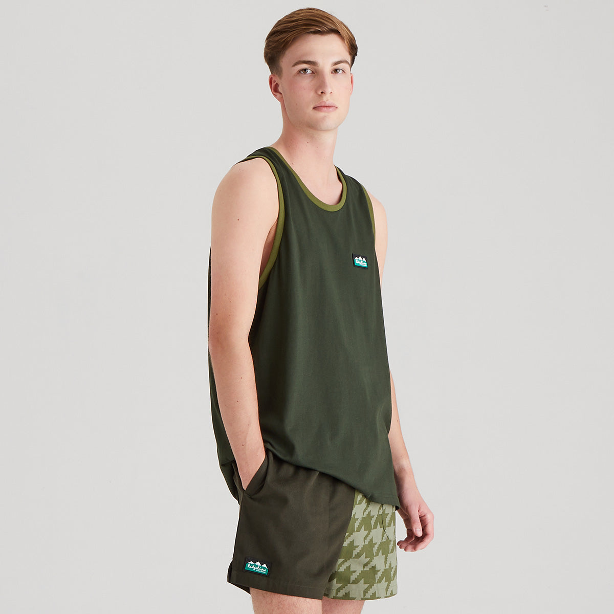 Man wearing a green tank top and shorts with a logo on a gray background