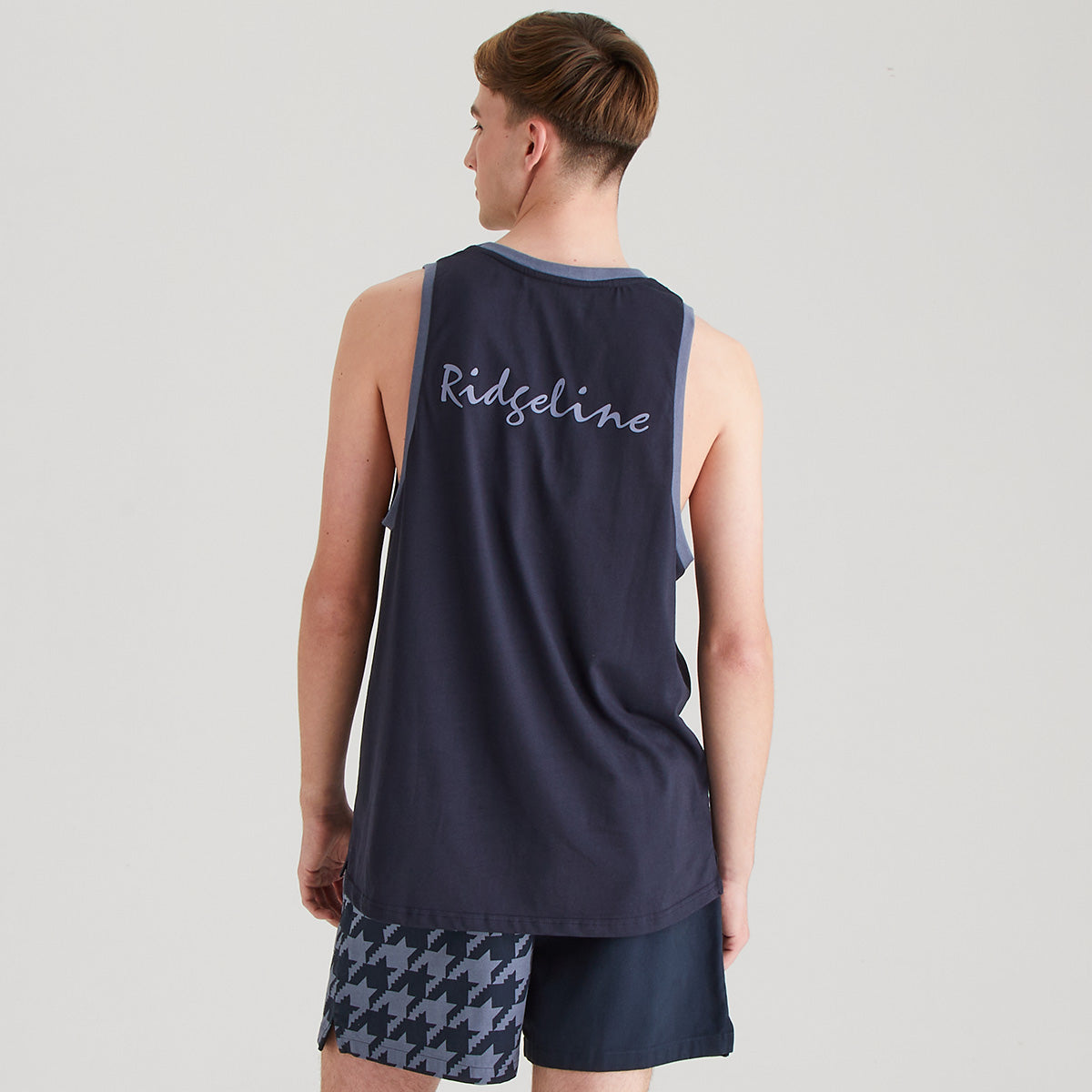 Person wearing a navy tank top with 'Ridgeline' branding and checkered shorts on a light gray background