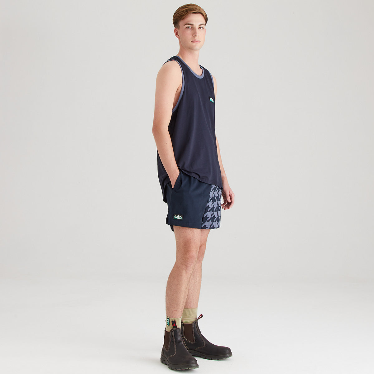 Person wearing a navy tank top and patterned shorts on a light gray background