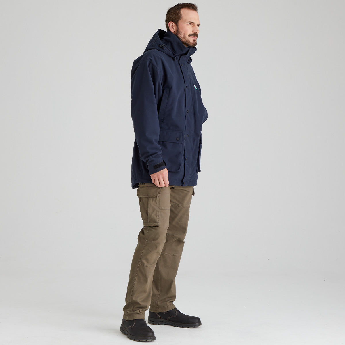 Man wearing a navy blue waterproof jacket and brown pants on a grey background