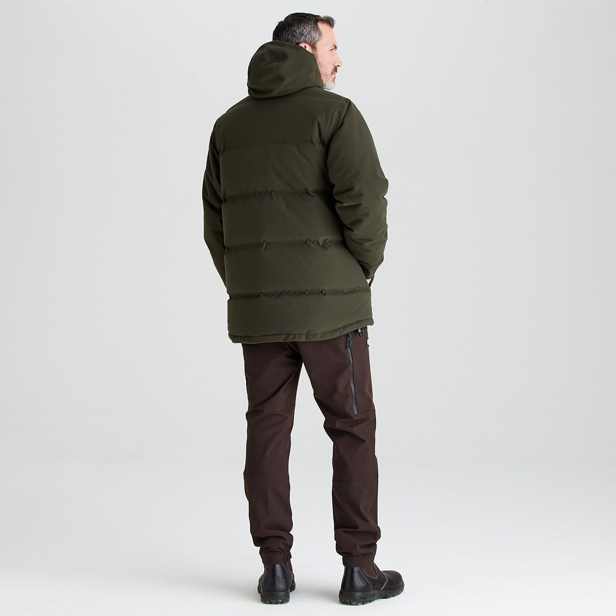 Man wearing a green puffer jacket and brown pants on a light gray background