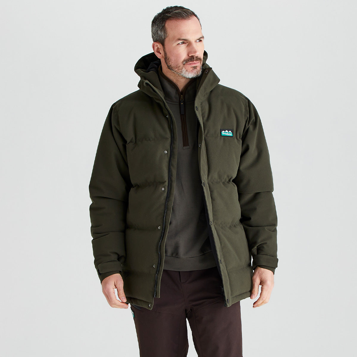 Man wearing a green jacket with a visible brand logo on a light gray background