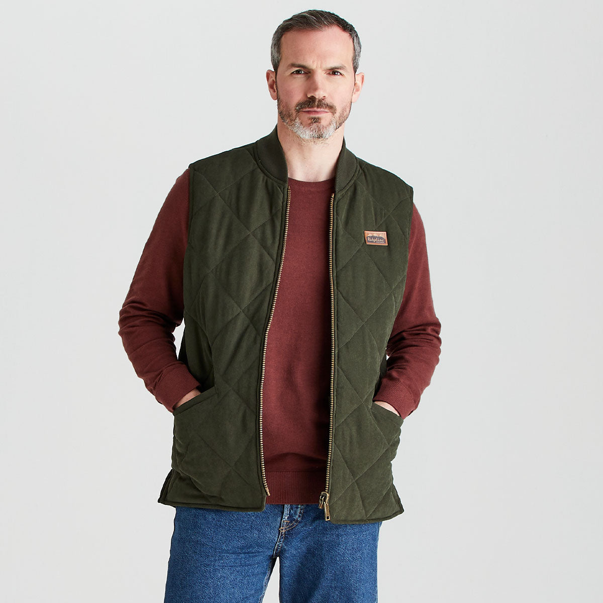 Man wearing a green quilted vest over a red t-shirt with a white background