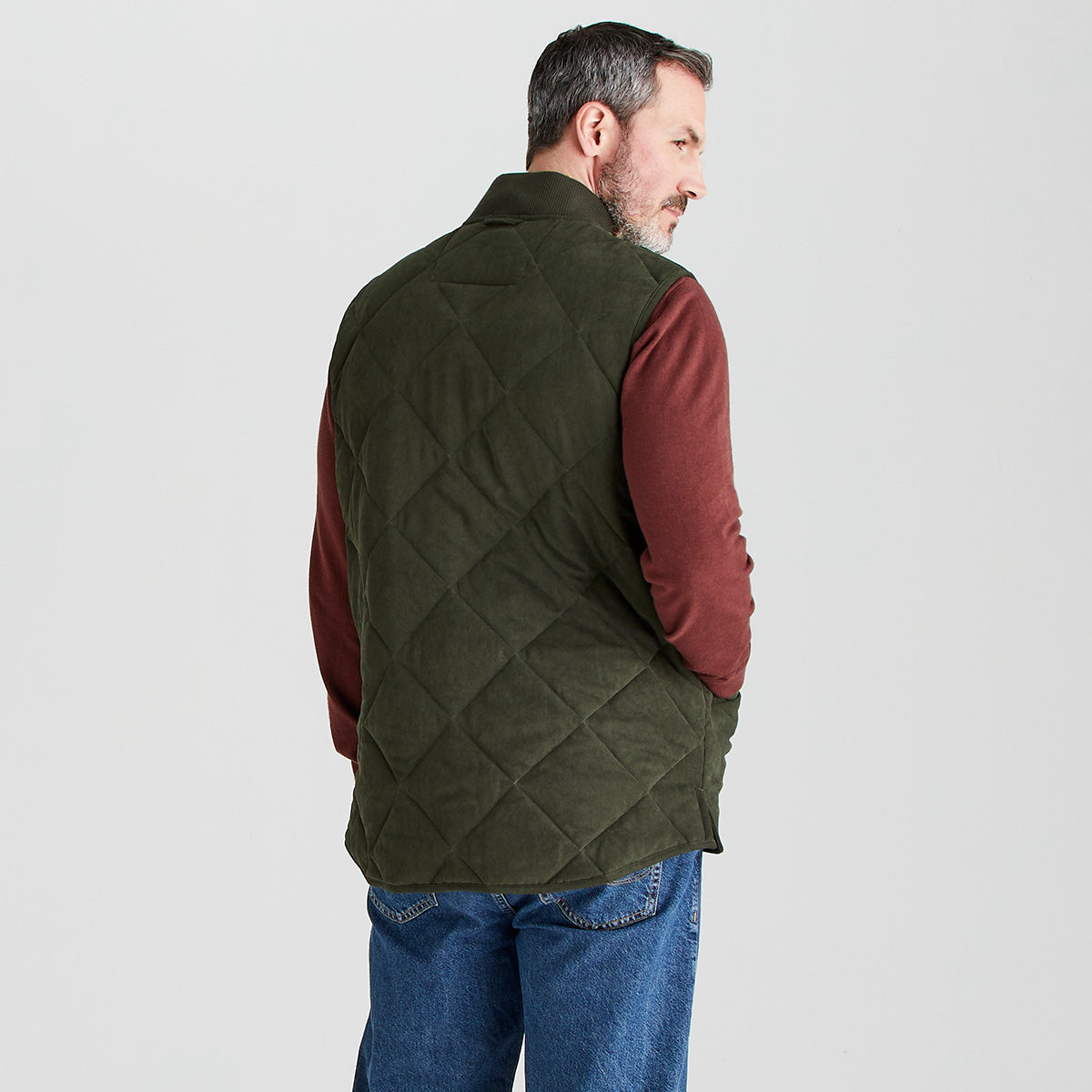 Man wearing a green quilted vest over a red shirt on a light gray background