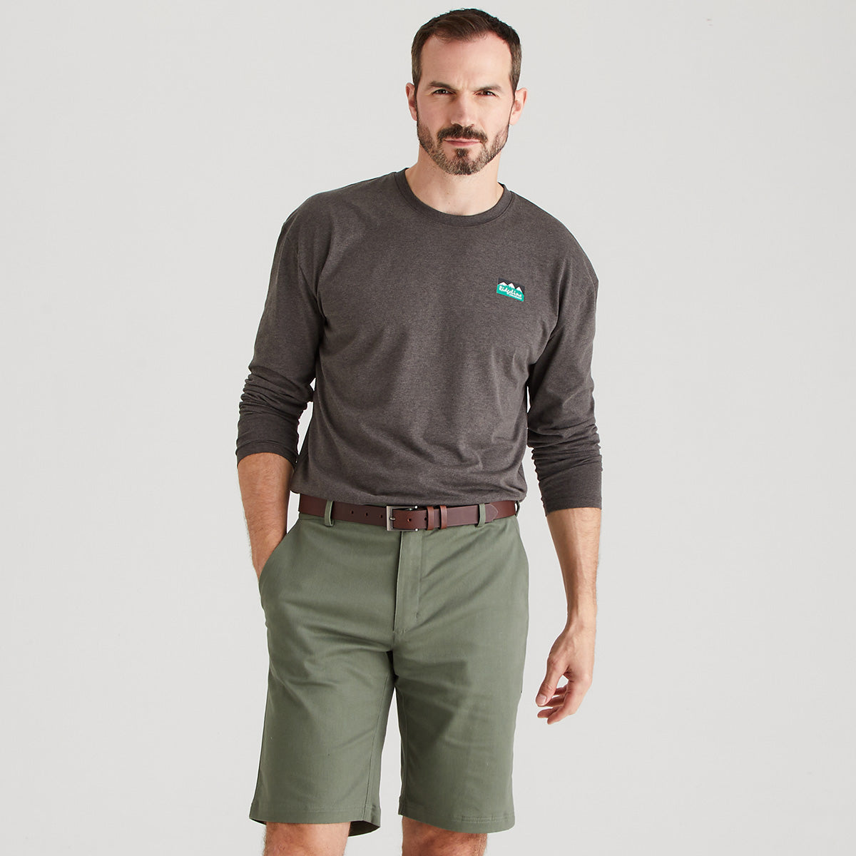 Man wearing a dark gray long-sleeve shirt with a logo and green shorts on a light gray background