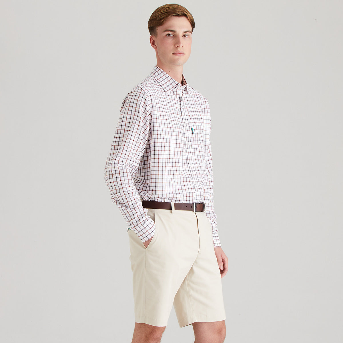 Man wearing a checkered shirt and beige shorts on a gray background