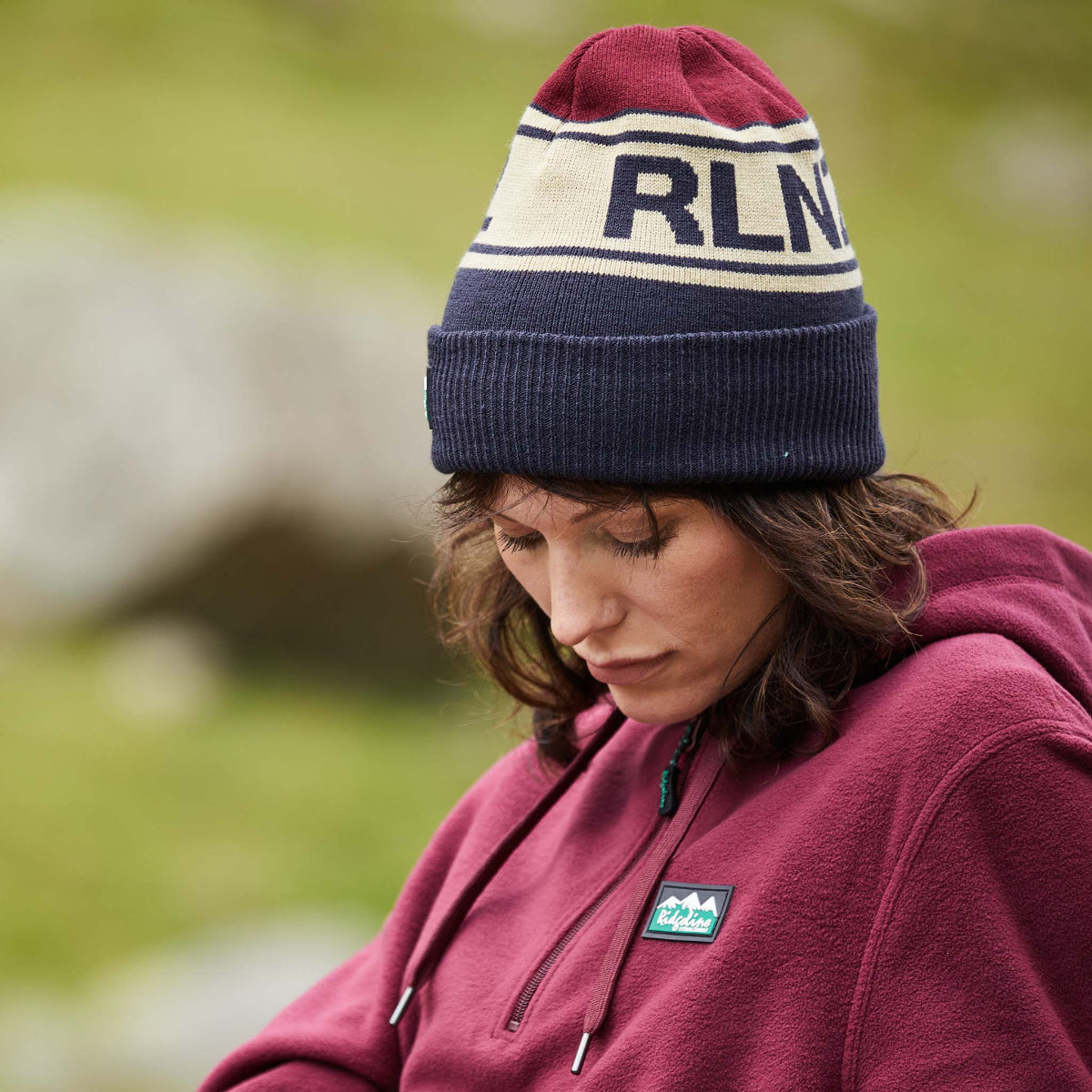 Person wearing a maroon beanie with 'RLNZ' branding and a matching jacket outdoors.