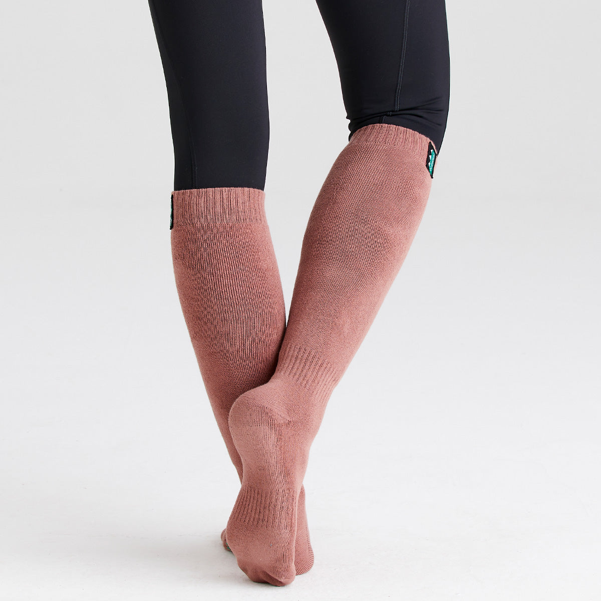 Dusty pink knee-high cotton work socks worn with crossed legs, featuring a ribbed knit design and full-length coverage for warmth and comfort.